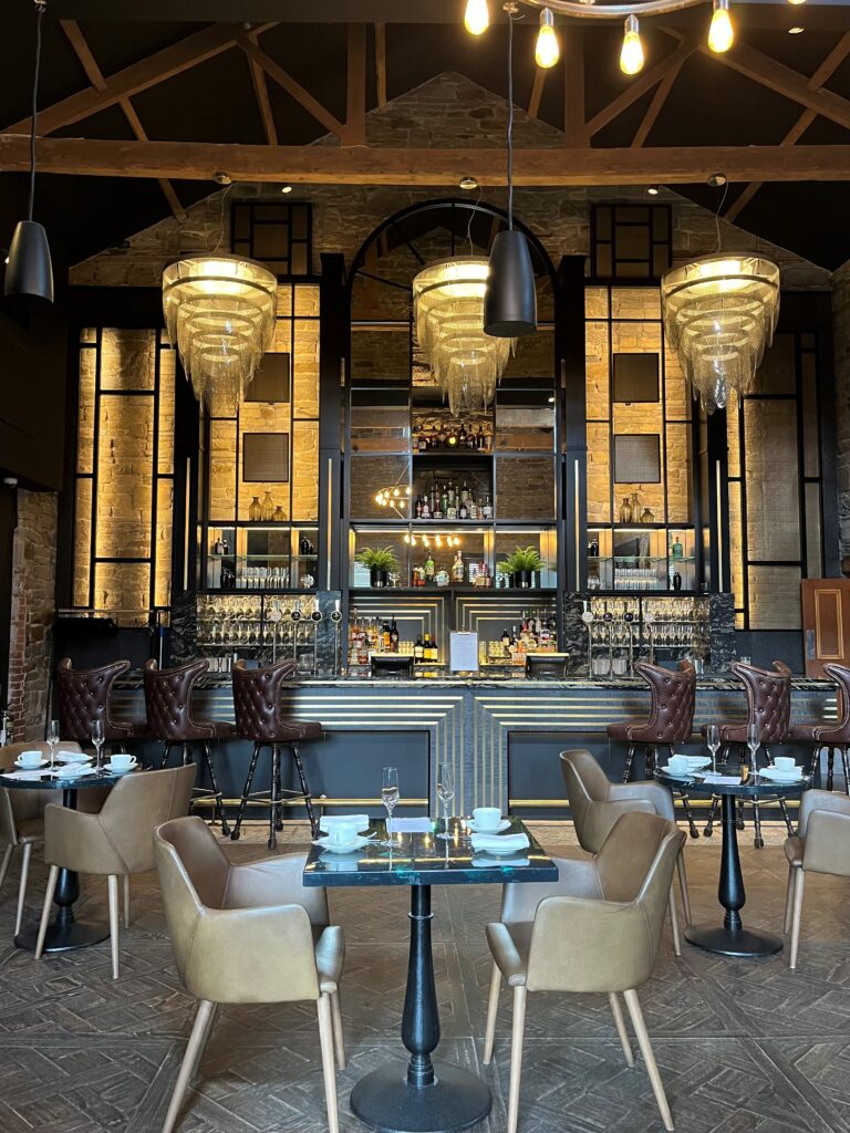 An inside view of the Coach House looking towards the bar area with seating and three impressive chandeliers.