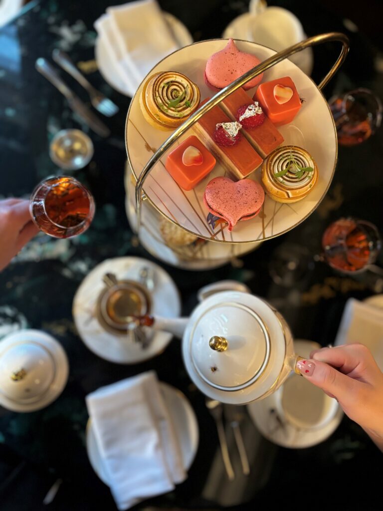 A close-up picture of Valentine's Afternoon Tea with sweet treats on a three-tier stand, teapot, and glass of fizz.
